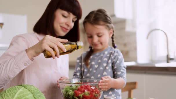 Ritratto di mamma sorridente e figlioletta aggiunge olio d'oliva all'insalata durante la cottura in cucina — Video Stock