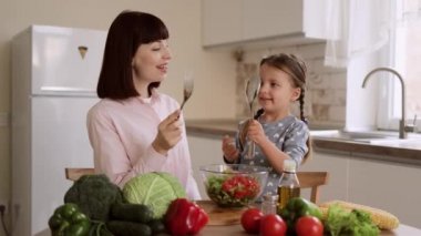 Genç beyaz anne ve küçük anaokulu kızı kaşık ve çatal kullanarak kavga ederken eğleniyorlar.