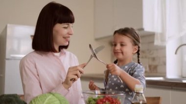 Genç beyaz anne ve küçük anaokulu kızı kaşık ve çatal kullanarak kavga ederken eğleniyorlar.