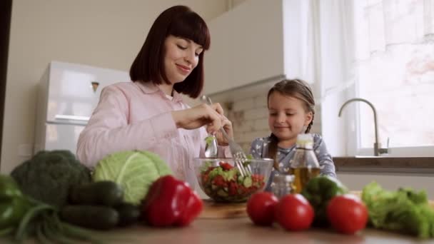 Malá dcera pomáhá mladé matce vařit zdravou večeři v moderním útulném světle domácí kuchyně — Stock video