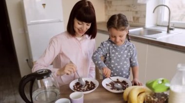 Genç anne ve küçük tatlı kız, mutfak masasında oturmuş, kahvaltının tadını çıkarıyor.
