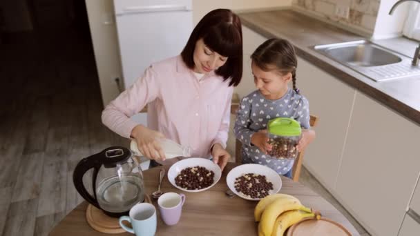Młoda mama i szczęśliwy mało słodkie córeczka siedzi przy stole w kuchni i korzystających śniadanie — Wideo stockowe