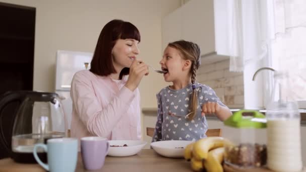 Charmant moeder en haar dochtertje voeden elkaar met chocolade maïs ballen met melk — Stockvideo