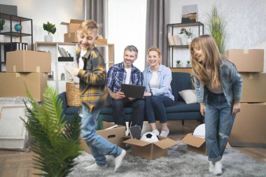 Mutlu ebeveynler dizüstü bilgisayar kullanırken iki çocuk yeni bir dairede oynuyor.