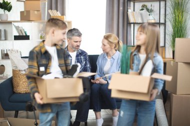 Taşınan kutularla gülümseyen çocuklar yeni dairede poz veriyorlar.