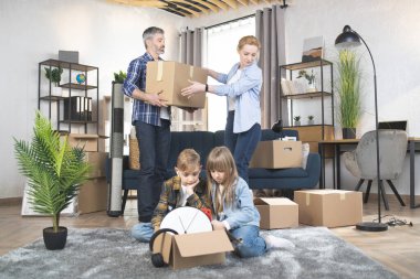 Ebeveynler kutuları toplarken iki küçük çocuk oyun oynuyor.