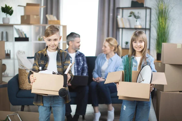 Niños sonrientes con cajas móviles posando en un piso nuevo con padres detrás — Foto de Stock