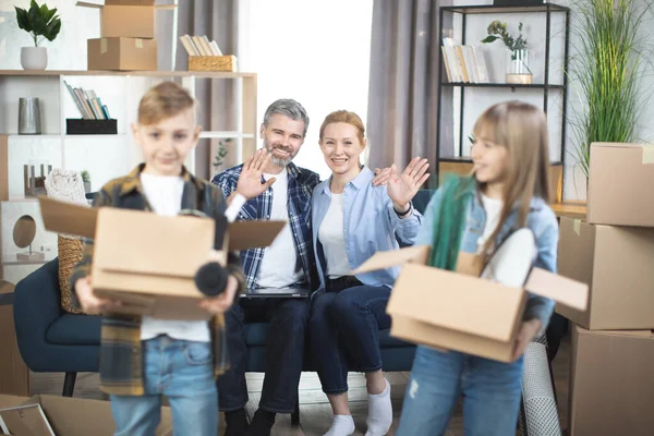 Niños sonrientes con cajas móviles posando en un piso nuevo con padres detrás — Foto de Stock