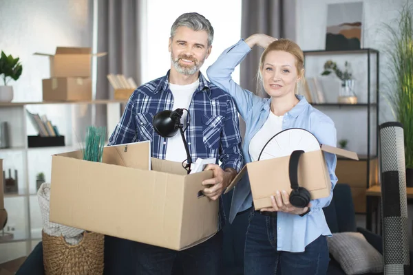 Caucásico pareja madura sonriendo y abrazando a su nuevo piso, sosteniendo cajas de cartón — Foto de Stock
