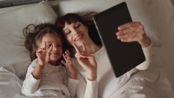 Mujer madre con su hija leyendo tableta digital en la cama blanca. — Vídeo de stock