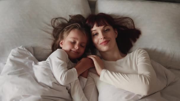Gülümseyen Kafkas anne ve kızı evde birlikte rahatlar, yatakta uzanırlar.. — Stok video