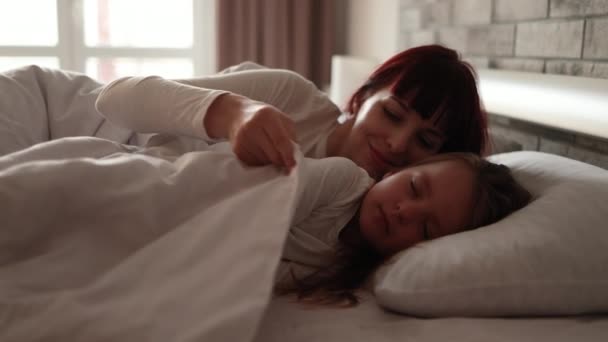 Bonito menina criança dorme na cama, enquanto sua mamãe ajustando o cobertor e acaricia o cabelo — Vídeo de Stock