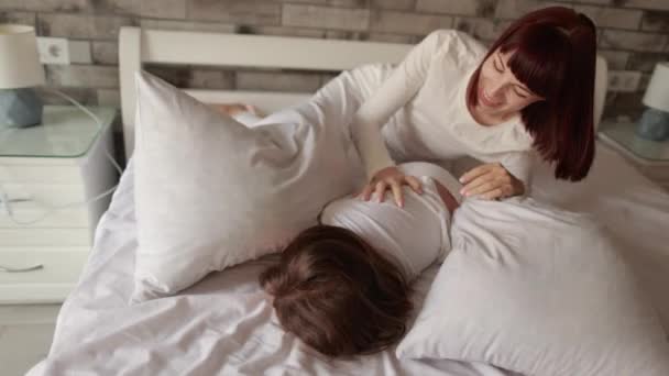 白种人妈妈抱着枕头和学龄前女儿打斗一起在床上玩乐 — 图库视频影像