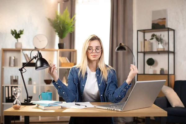 Female freelancer in eyeglasses meditating at table, feeling relaxed Stock Image