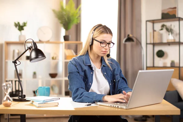 Mooie jonge vrouw met behulp van headset en laptop voor video-oproep, werken thuis — Stockfoto