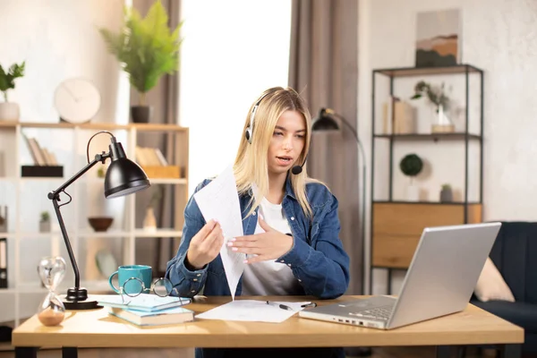 Blond woman in headset and casual clothes having video chat on laptop, working from home or bright office —  Fotos de Stock