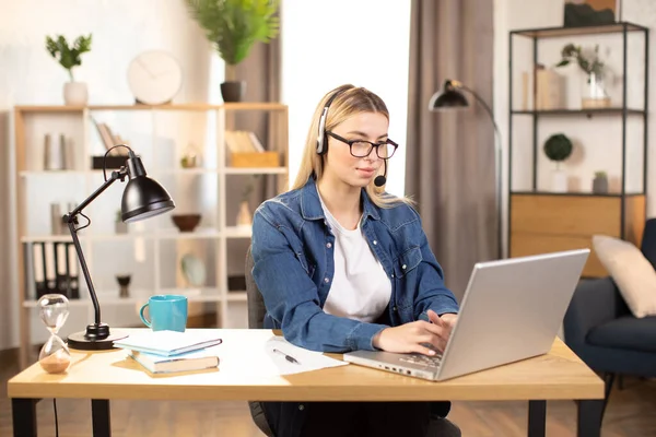 Wanita muda cantik menggunakan headset dan laptop untuk panggilan video, bekerja di rumah — Stok Foto