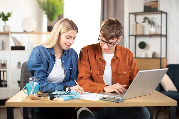 Молодий чоловік і жінка використовують ноутбук, сидячи за столом і навчаючись разом — стокове фото