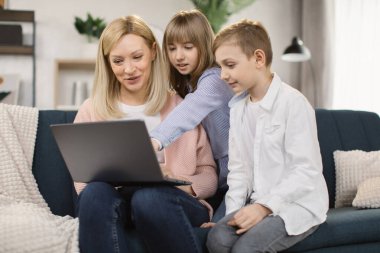 Mutlu bir anne, küçük bir oğul ve kız ailesi rahat bir kanepede oturup dizüstü bilgisayar kullanıyor.