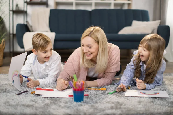 Küçük çocuklar ve anneleri oturma odasında yerde yatıp renkli kalemlerle resim yapıyorlar. — Stok fotoğraf