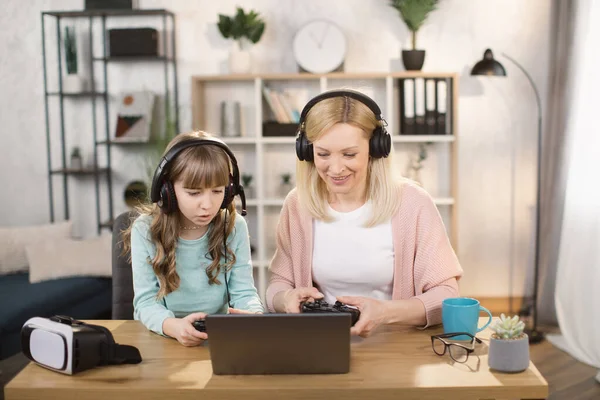 Kind dochter en moeder spelen video games met behulp van joysticks op laptop samen thuis. — Stockfoto