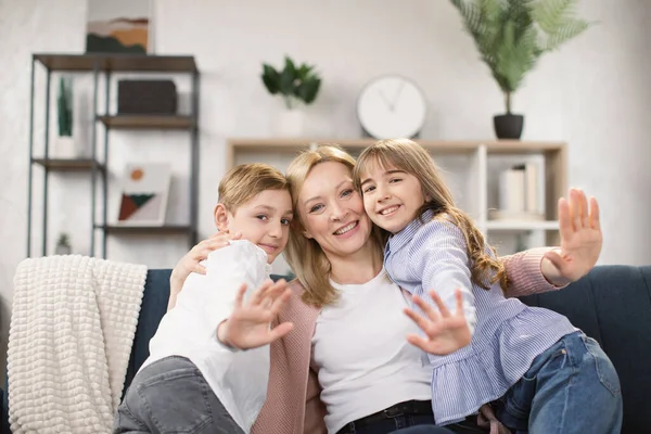 Feliz madre divirtiéndose con dos niños pequeños en casa, sentados en un acogedor sofá en la sala de estar — Foto de Stock