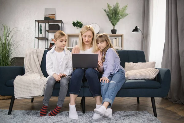 Single Caucasian mother and little children sitting on couch using laptop — стокове фото