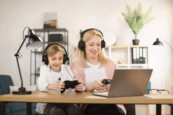 Kind zoon en moeder spelen video games met behulp van joysticks op laptop samen thuis. — Stockfoto