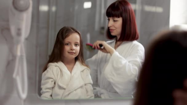 Loving mom brushing hair of cute little girl in the bathroom. — Vídeo de stock