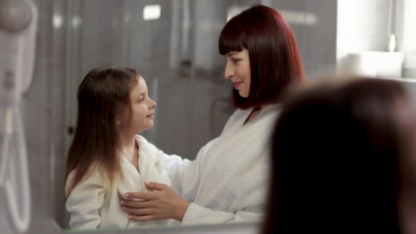 Kaukasiska mor och dotter i badrockar gör frisyrer i badet — Stockvideo