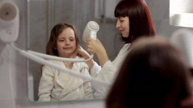 Anne duştan sonra çocuk saçlarını fırçalıyor ve kurutuyor. Kız aynaya bakıyor..