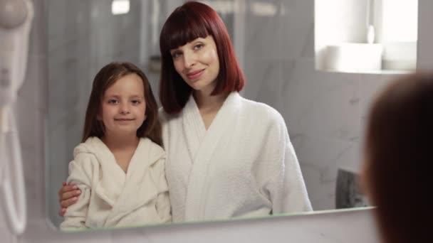Mor och dotter i vita badrockar står i badrummet under förmiddagen förfaranden — Stockvideo