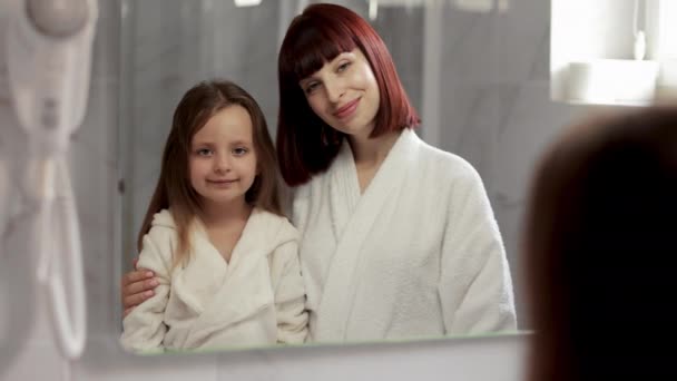 Anne ve kız, sabahları banyoda beyaz bornozla dikiliyorlar. — Stok video