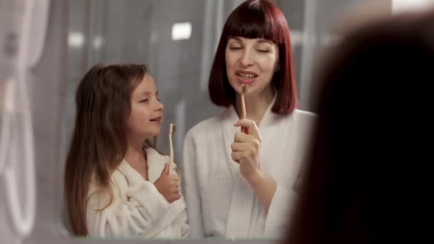 Mother and her little cute looking at mirror and singing at toothbrush like in microphone — Wideo stockowe
