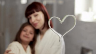 Anne ve kız, sabahları banyoda beyaz bornozla dikiliyorlar.