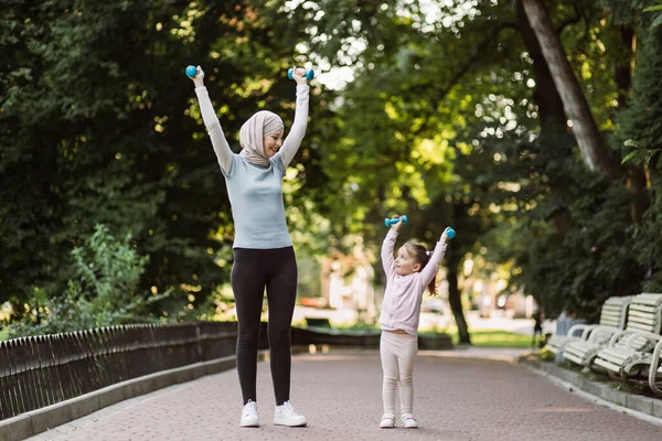 Mulher muçulmana e sua filha criança fazendo exercícios de fitness com halteres em um parque — Fotografia de Stock