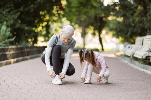 Mãe árabe e sua filha ajustando tênis, sentado na pista de jogging no parque — Fotografia de Stock