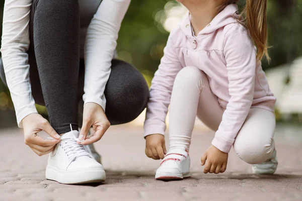 Anne ve kızının spor ayakkabılarını ayarlarken, parkta koşu pistinde otururken kesilen görüntüleri. — Stok fotoğraf