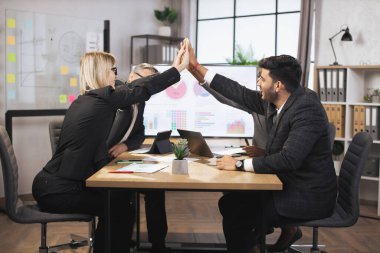 Çok ırklı iş adamlarından oluşan başarılı bir ekip toplantı odasında toplanırken beşlik çakıyor.