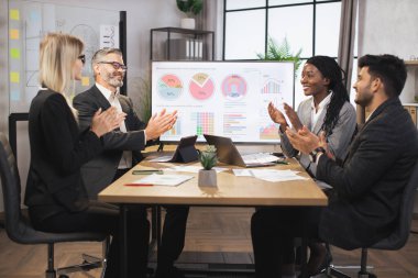 Uluslararası şirket çalışanlarından oluşan bir ekip birlikte çalışırken masada oturuyor ve alkışlıyorlar.