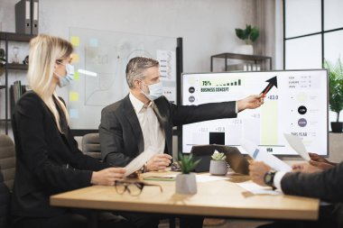 Yüz maskesi takmış olgun bir şef, odaklanmış uluslararası meslektaşlarıyla toplantı yapıyor.