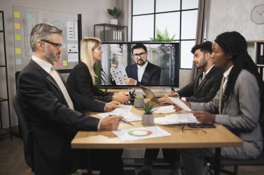 Özgüvenli sakallı beyaz adam çok uluslu meslektaşlarına iş programı kavramını anlatıyor.