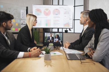Konferans odasında odaklanmış çok ırklı iş adamları dizüstü bilgisayara bakıyor, video konferansı yapıyorlar.