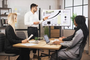 Takım elbiseli Hintli yönetici, iş arkadaşlarıyla ofisinde konuşuyor.