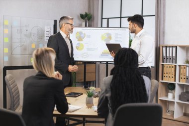 Karışık ırk iş adamlarından oluşan bir ekip orta yaşlı erkek sakallı şeflerini dinliyor.