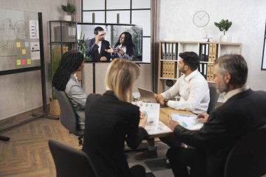 Çeşitli etnik çeşitlilikte dört iş adamından oluşan bir ekip toplantı odasında video toplantısı yapıyor.