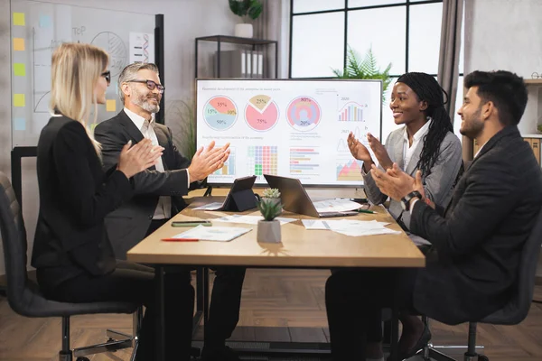 Uluslararası şirket çalışanlarından oluşan bir ekip birlikte çalışırken masada oturuyor ve alkışlıyorlar.