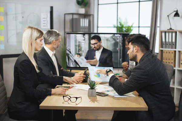 Uluslararası ortaklardan oluşan bir grup modern toplantı odasında ortak projenin detaylarını tartışıyor.