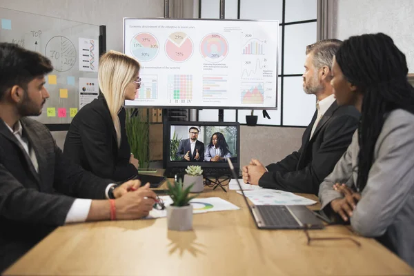 Konferans odasında odaklanmış çok ırklı iş adamları dizüstü bilgisayara bakıyor, video konferansı yapıyorlar.