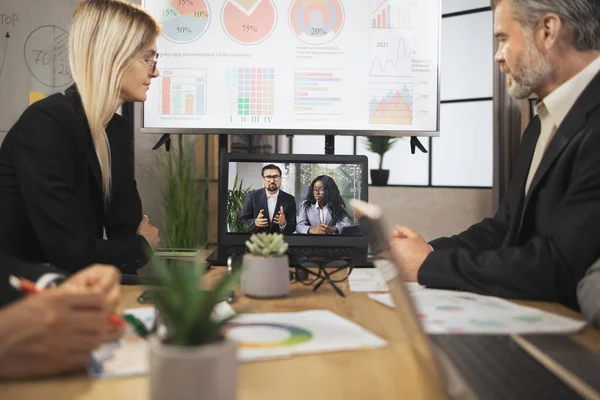 Konferans odasında odaklanmış çok ırklı iş adamları dizüstü bilgisayara bakıyor, video konferansı yapıyorlar.